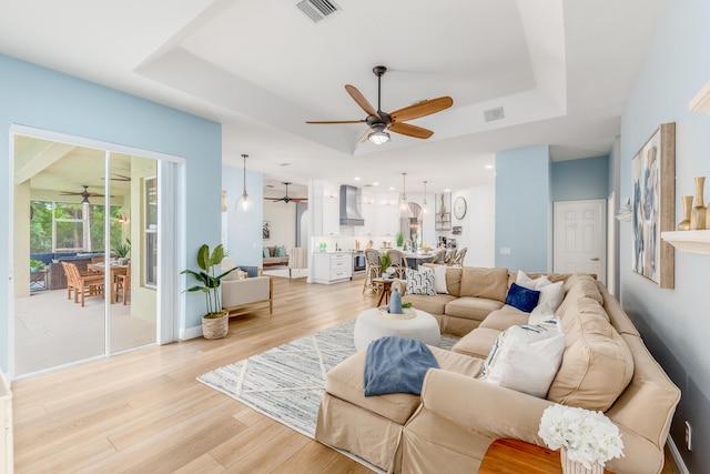 living area with visible vents, a raised ceiling, a ceiling fan, light wood-style floors, and recessed lighting