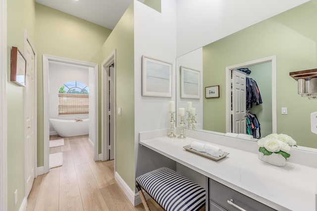 bathroom with a freestanding tub, wood finished floors, vanity, baseboards, and a spacious closet