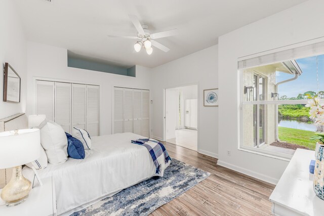 bedroom with baseboards, a ceiling fan, a water view, light wood-type flooring, and multiple closets