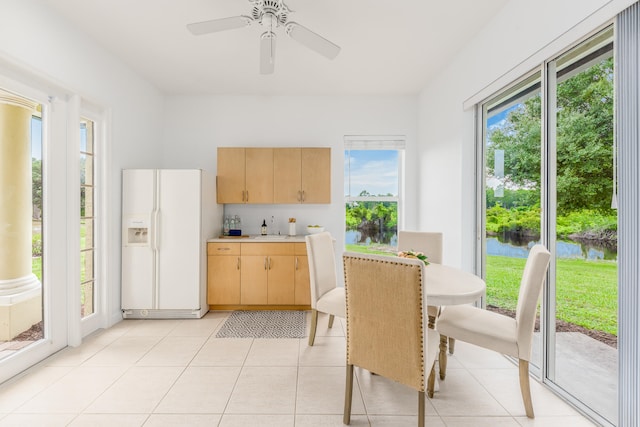 kitchen with ceiling fan, white refrigerator with ice dispenser, light brown cabinets, light tile patterned floors, and a water view