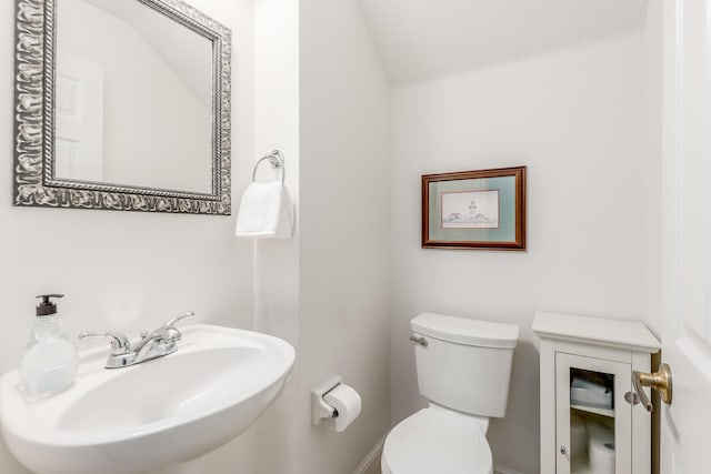 half bath featuring toilet, vaulted ceiling, and a sink