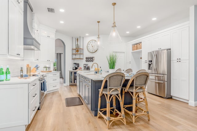 kitchen with white cabinets, light countertops, appliances with stainless steel finishes, a center island with sink, and pendant lighting