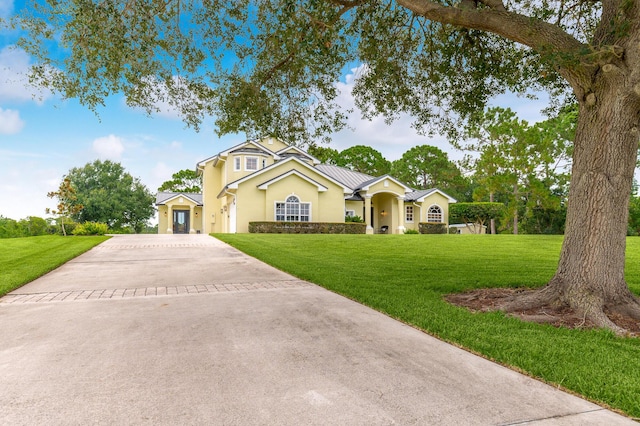 view of front of property featuring a front yard, concrete driveway, metal roof, and stucco siding