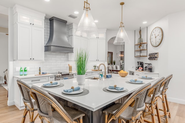 kitchen featuring custom exhaust hood, a center island with sink, electric stove, light hardwood / wood-style flooring, and white cabinetry