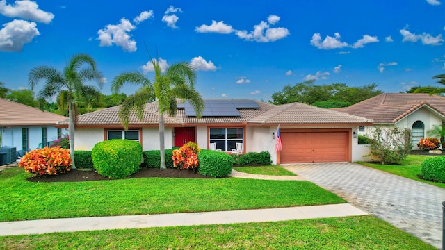 view of front of house featuring a garage, solar panels, cooling unit, and a front lawn