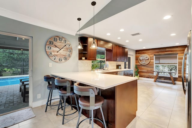 kitchen featuring a healthy amount of sunlight, decorative light fixtures, kitchen peninsula, and wood walls