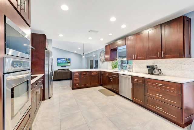 kitchen with pendant lighting, lofted ceiling, appliances with stainless steel finishes, backsplash, and kitchen peninsula