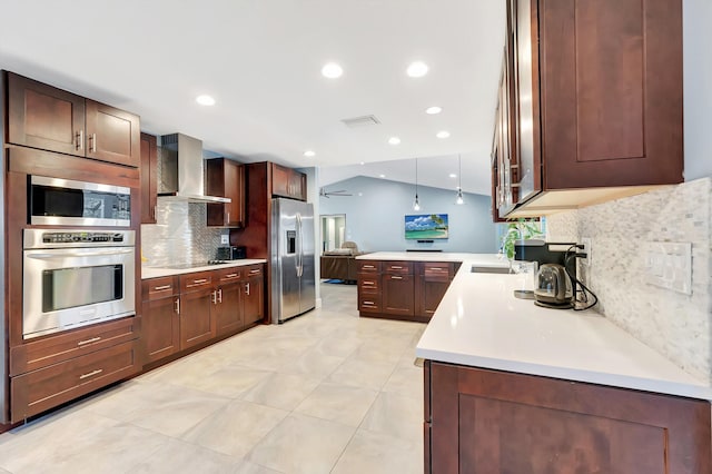 kitchen featuring lofted ceiling, kitchen peninsula, pendant lighting, stainless steel appliances, and wall chimney range hood