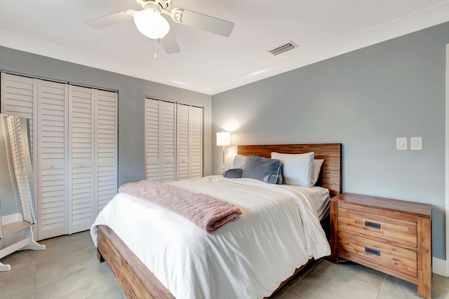 bedroom with light tile patterned flooring, ceiling fan, ornamental molding, and two closets