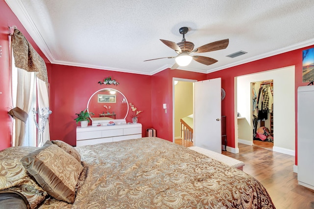 bedroom featuring ceiling fan, ornamental molding, a walk in closet, a closet, and light hardwood / wood-style floors