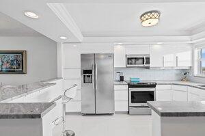 3212 S Ocean Blvd Unit 807-A, Highland Beach, FL 33487 - kitchen with a peninsula, light tile patterned floors, stainless steel appliances, white cabinets, and ornamental molding