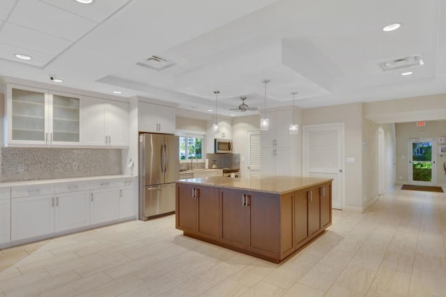 kitchen featuring pendant lighting, light stone counters, white cabinets, appliances with stainless steel finishes, and a center island