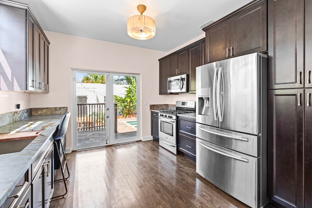 kitchen with appliances with stainless steel finishes, dark hardwood / wood-style flooring, stone countertops, and dark brown cabinets