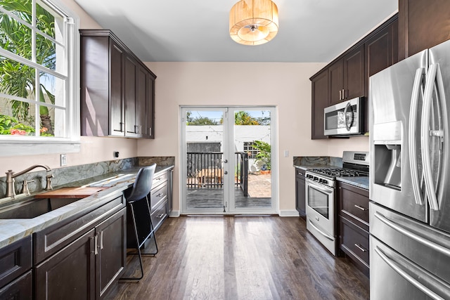 kitchen featuring dark brown cabinetry, stainless steel appliances, dark wood-type flooring, sink, and stone countertops