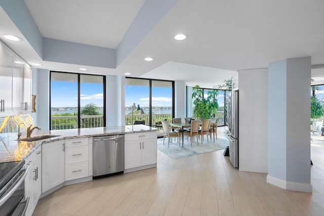 kitchen with white cabinets, appliances with stainless steel finishes, light stone counters, a sink, and recessed lighting