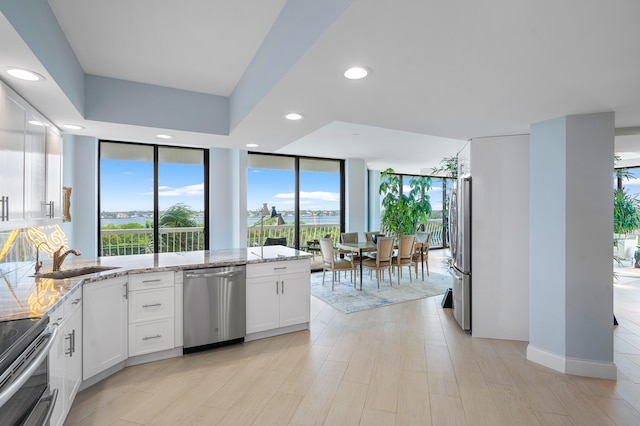 kitchen with appliances with stainless steel finishes, white cabinetry, light stone counters, and a wealth of natural light