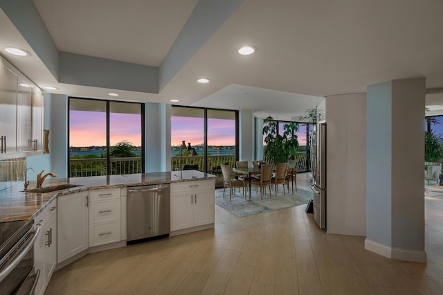 kitchen featuring stainless steel appliances, a sink, white cabinetry, light wood-style floors, and light stone countertops