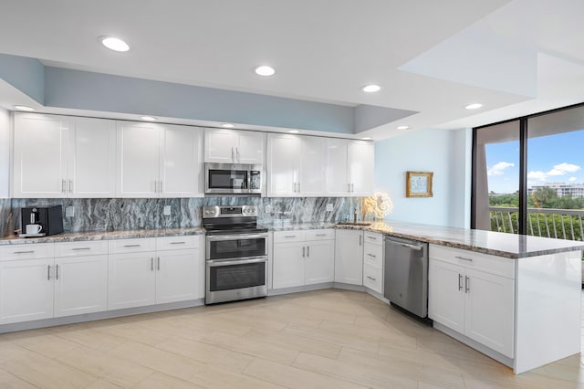 kitchen featuring light stone counters, stainless steel appliances, decorative backsplash, white cabinetry, and a peninsula