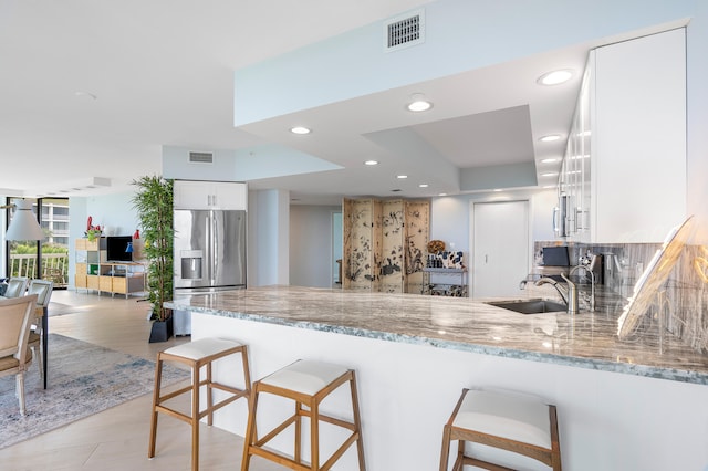 kitchen featuring a kitchen breakfast bar, kitchen peninsula, stainless steel appliances, white cabinetry, and light stone counters