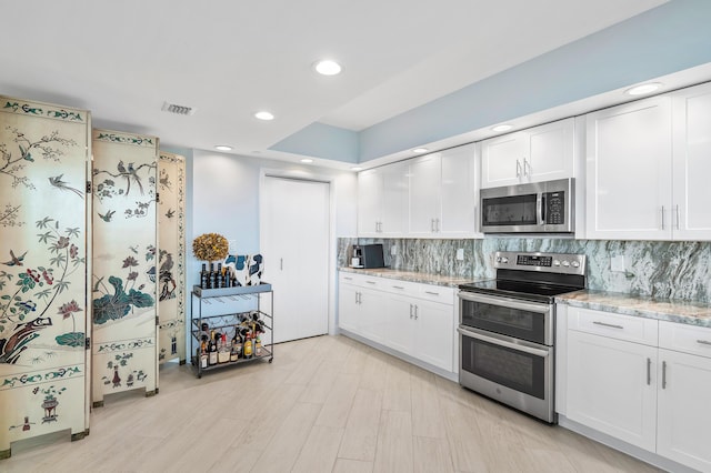 kitchen with light stone counters, stainless steel appliances, tasteful backsplash, visible vents, and white cabinets