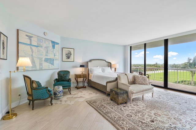 bedroom with expansive windows, access to outside, wood finished floors, and baseboards