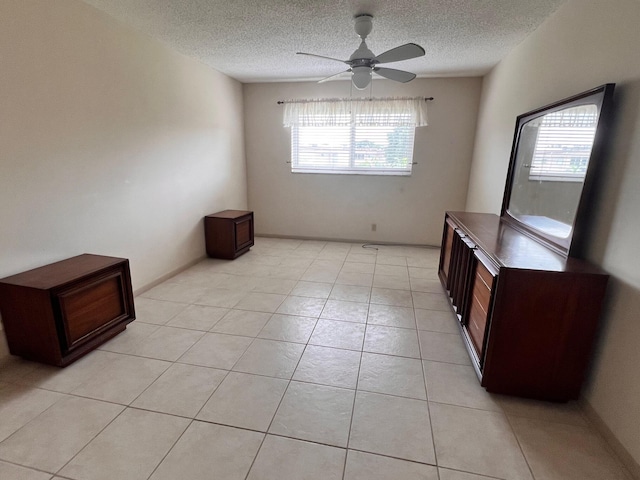 tiled empty room with ceiling fan, a wealth of natural light, and a textured ceiling