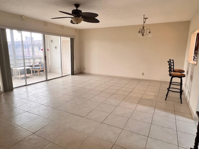 empty room featuring ceiling fan with notable chandelier, light tile patterned flooring, and a textured ceiling