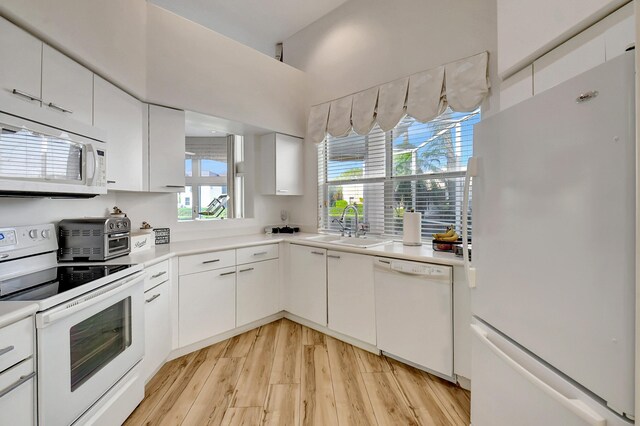 kitchen featuring white appliances, white cabinetry, light countertops, and a sink