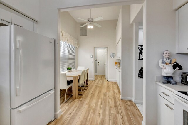 kitchen with light countertops, light wood-style flooring, a towering ceiling, white cabinets, and white appliances