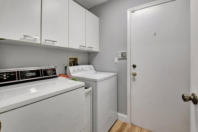 laundry room featuring washing machine and clothes dryer, light hardwood / wood-style floors, and cabinets