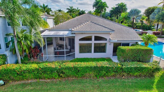 back of house featuring a sunroom, a tiled roof, and stucco siding