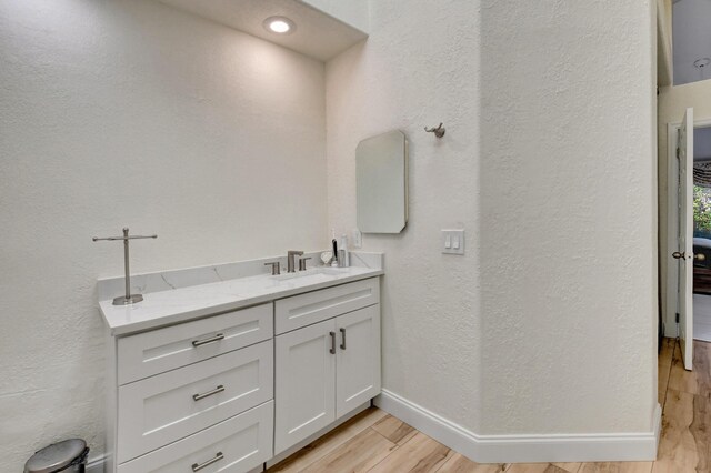 bathroom featuring a textured wall, baseboards, wood finished floors, and vanity