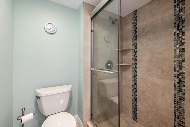 bathroom featuring a shower with door and toilet