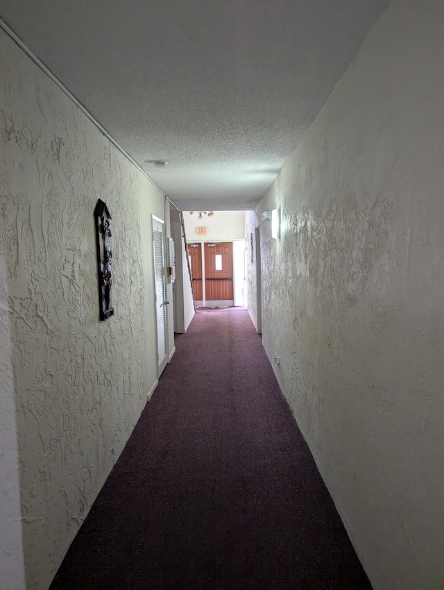 hall featuring a textured ceiling, carpet, and a textured wall