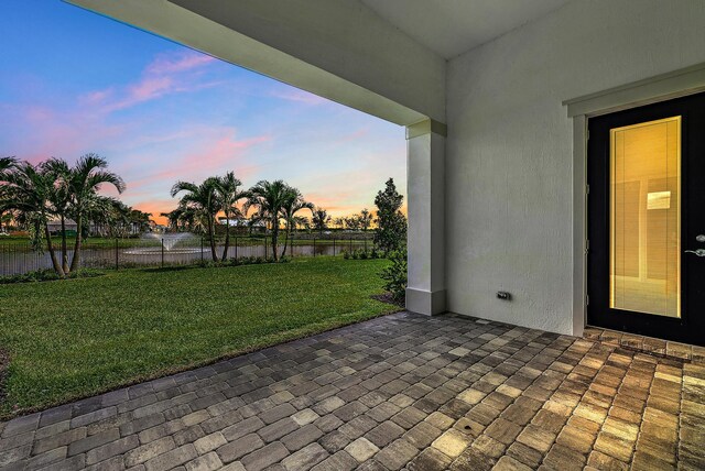 patio terrace at dusk featuring a lawn