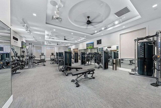 exercise room with rail lighting, ceiling fan, a raised ceiling, and light colored carpet