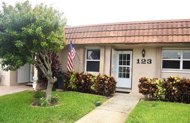 doorway to property with a tile roof, a yard, and stucco siding