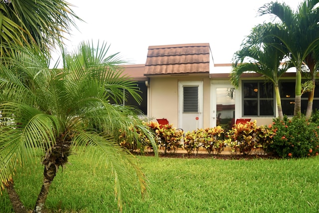 view of side of home featuring stucco siding, a lawn, and a tile roof