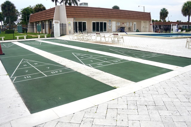 view of community featuring a patio, shuffleboard, and fence