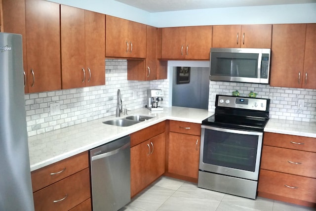 kitchen with backsplash, light countertops, brown cabinets, appliances with stainless steel finishes, and a sink