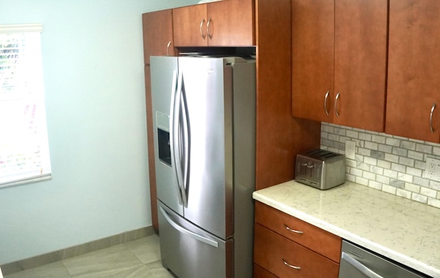 kitchen with light tile patterned floors, brown cabinetry, baseboards, appliances with stainless steel finishes, and backsplash