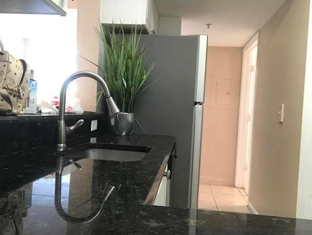 kitchen featuring light tile patterned floors, sink, dark stone counters, white cabinetry, and stainless steel refrigerator