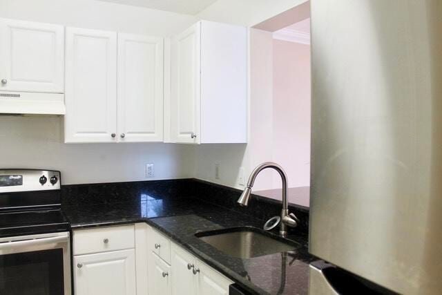 kitchen with dark stone countertops, white cabinets, range hood, sink, and range