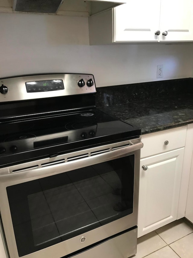 kitchen with stainless steel range with electric stovetop, white cabinets, light tile patterned floors, and custom range hood