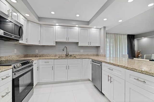 kitchen with appliances with stainless steel finishes, white cabinetry, sink, a tray ceiling, and light stone countertops