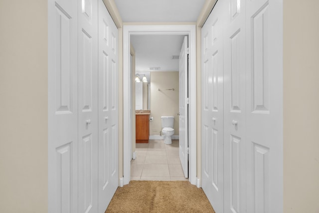 corridor with baseboards, light tile patterned flooring, visible vents, and light colored carpet