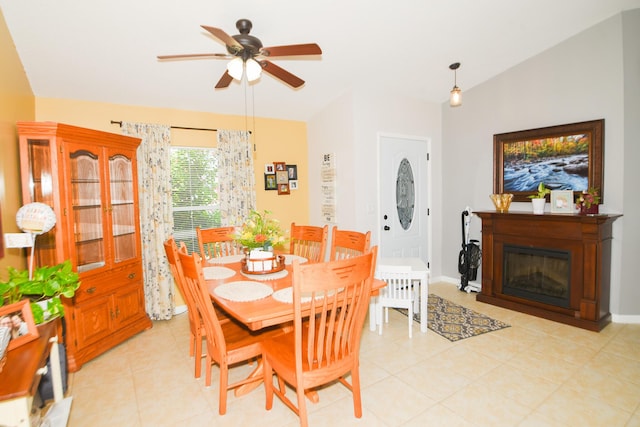 dining area featuring ceiling fan, light tile patterned floors, a glass covered fireplace, and baseboards