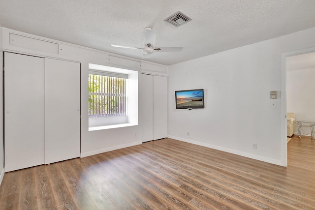 unfurnished bedroom with a textured ceiling, two closets, dark hardwood / wood-style floors, and ceiling fan