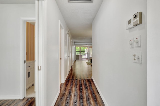 corridor with a textured ceiling and dark hardwood / wood-style floors