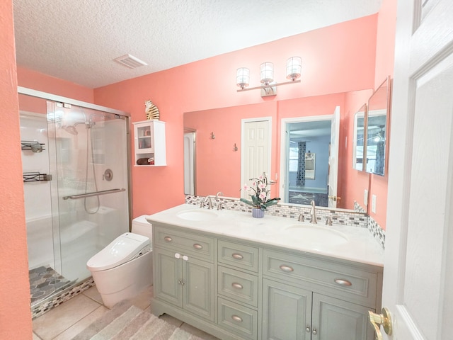 bathroom featuring a shower with door, tile patterned flooring, a textured ceiling, toilet, and dual bowl vanity